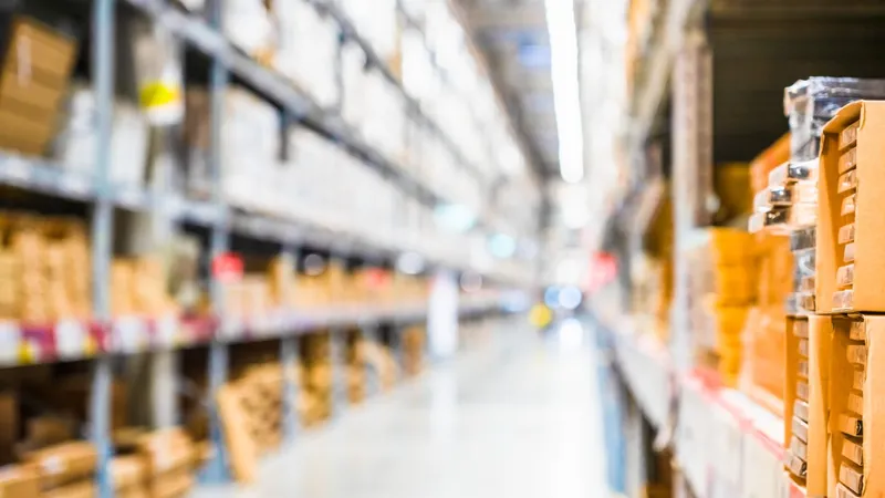 Pasillo de una bodega de almacenamiento con estanterías metálicas cargadas de cajas de cartón apiladas a ambos lados, en perspectiva y con enfoque selectivo en las cajas del primer plano