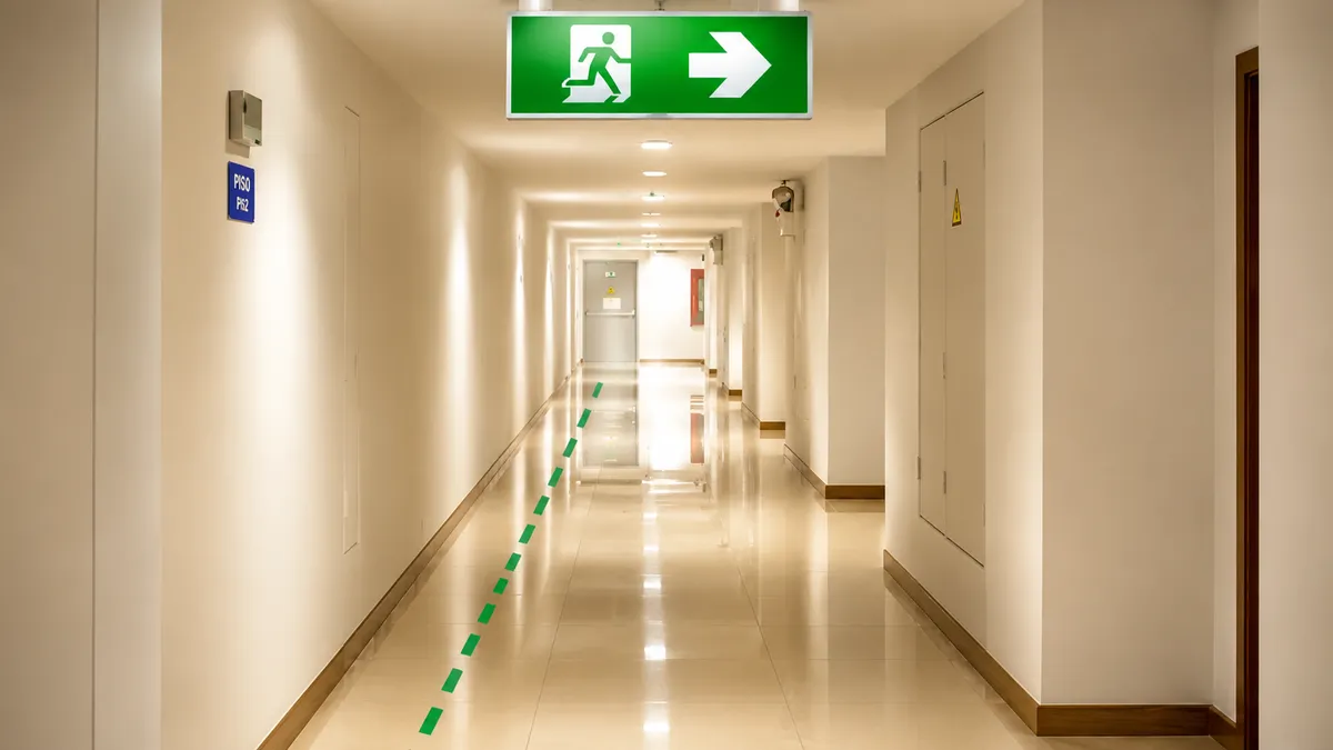 Detalle de una escalera de evacuación presurizada en un edificio de gran altura, con una puerta cortafuego entreabierta, señalización fotoluminiscente en el zócalo y luces de emergencia en la pared